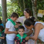 Cinthia Palomino, Auxiliar da Novo Encanto no Núcleo Grande Ventura, e Christiane Pescarmona, Responsável Nuclear pela OE no Núcleo Grande Ventura, entregando os lenços e botons para as crianças do Núcleo.